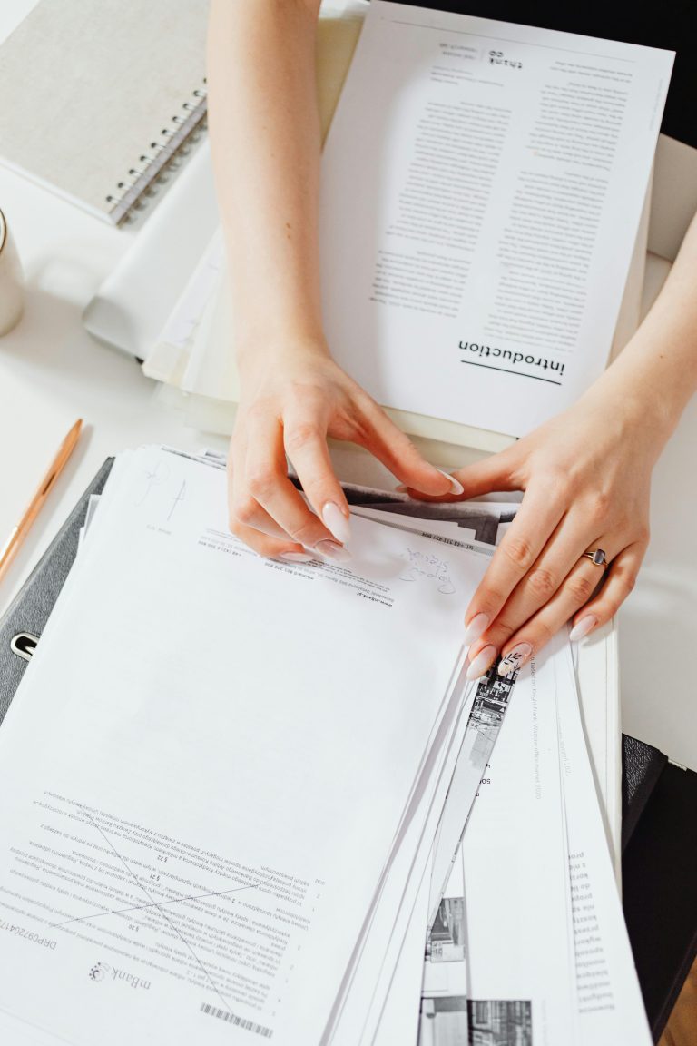 Close-up of a woman's hands managing paperwork on a desk, showcasing organization skills.